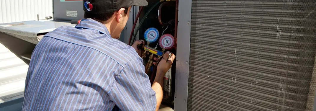 HVAC technician servicing a condenser unit in St. James
